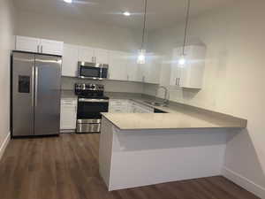 Kitchen with appliances with stainless steel finishes, white cabinetry, a peninsula, and hanging light fixtures