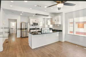 Kitchen with a peninsula, appliances with stainless steel finishes, white cabinets, light wood-style floors, and recessed lighting