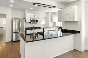 Kitchen featuring appliances with stainless steel finishes, a peninsula, white cabinetry, dark wood-type flooring, and dark stone counters