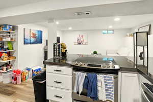 Kitchen with stainless steel appliances, white cabinetry, recessed lighting, light wood-style flooring, and dark stone counters