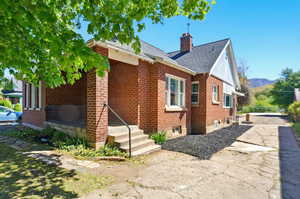 View of property exterior with brick siding, a chimney, and roof with shingles