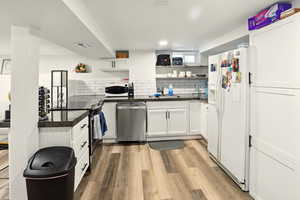 Kitchen with open shelves, appliances with stainless steel finishes, white cabinetry, and light wood finished floors