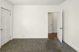 Unfurnished bedroom with dark colored carpet and baseboards