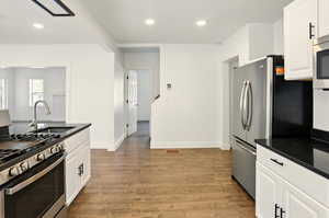 Kitchen with appliances with stainless steel finishes, white cabinets, recessed lighting, light wood finished floors, and dark stone countertops