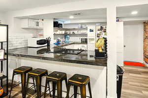 Kitchen with white appliances, white cabinets, light wood-type flooring, backsplash, and open shelves