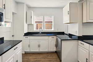 Kitchen with dark wood-type flooring, dark stone countertops, white cabinetry, and appliances with stainless steel finishes