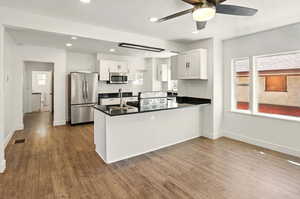 Kitchen with white cabinetry, appliances with stainless steel finishes, a peninsula, healthy amount of natural light, and recessed lighting