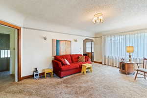Living room featuring plenty of natural light, arched walkways, carpet, and a textured ceiling