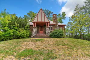 Tudor house featuring a front lawn, a chimney, and stone siding