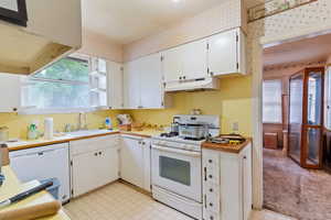 Kitchen with white appliances, light countertops, white cabinets, open shelves, and under cabinet range hood