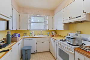 Kitchen with white appliances, under cabinet range hood, light countertops, light floors, and white cabinets
