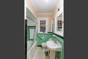 Bathroom with light tile patterned floors, shower / tub combo with curtain, tile walls, and a wainscoted wall