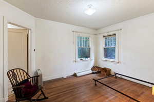 Unfurnished room with wood finished floors, a baseboard radiator, and a textured ceiling