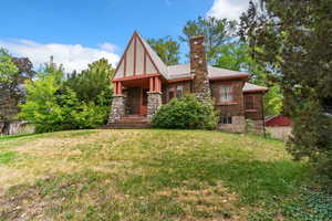 Tudor-style house with a front yard, a chimney, and stone siding