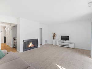 Living area with a warm lit fireplace and light colored carpet