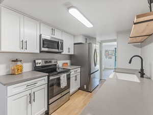 Kitchen with stainless steel appliances, light wood-style flooring, white cabinetry, and light stone counters