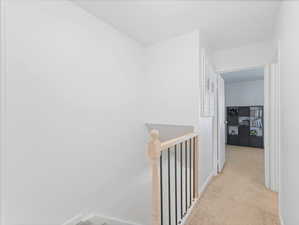 Hallway featuring an upstairs landing and light colored carpet