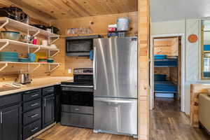 Kitchen featuring wooden walls, stainless steel refrigerator, dark wood-style floors, dark cabinets, and open shelves