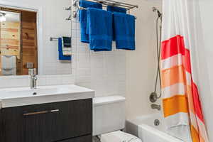 Bathroom featuring tile walls, shower / bath combo with shower curtain, vanity, and tasteful backsplash