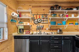 Kitchen with wood walls, stainless steel dishwasher, dark cabinets, open shelves, and light countertops
