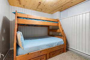 Unit 1b, bedroom featuring baseboard heating, wood walls, carpet, and wooden ceiling