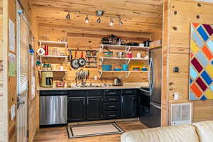 Kitchen featuring dark cabinetry, open shelves, wood walls, stainless steel appliances, and light countertops