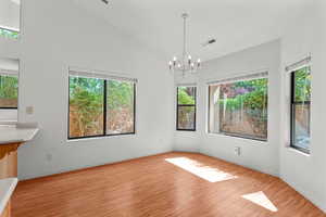 Unfurnished dining area with vaulted ceiling, a chandelier, and light wood-type flooring