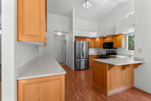 Kitchen featuring freestanding refrigerator, light wood-type flooring, light countertops, range with electric stovetop, and a peninsula