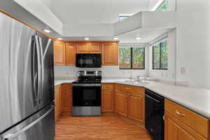 Kitchen featuring black appliances, light countertops, light wood-style flooring, recessed lighting, and brown cabinets