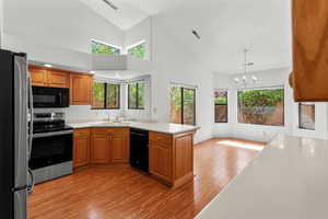 Kitchen with black appliances, high vaulted ceiling, light countertops, brown cabinets, and light wood-style flooring