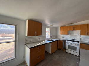 Kitchen featuring white gas range, dark LVP finished floors, backsplash, a textured ceiling, and brown cabinets