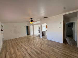 Unfurnished living room with arched walkways, light wood-type flooring, a ceiling fan, and a textured ceiling