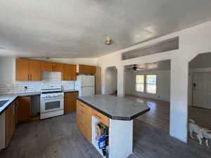 Kitchen featuring vaulted ceiling, arched walkways, white appliances, backsplash, and dark wood-style flooring