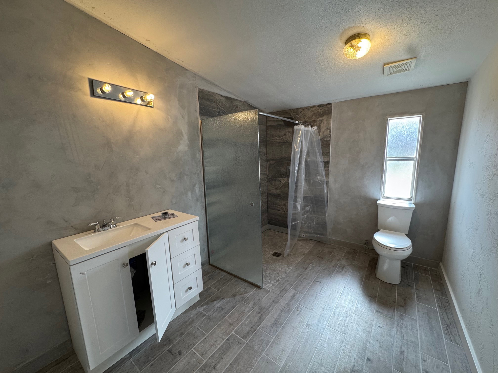 Bathroom with vanity, a textured ceiling, new floors, tiled shower, and a tile shower