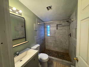 Full bathroom with vanity, a stall shower, a textured ceiling, a textured wall, and LVP finished floors
