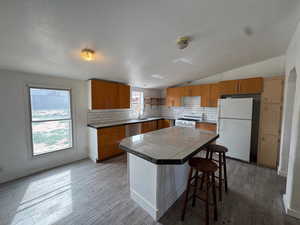 Kitchen with tasteful backsplash, wood finish cabinetry, white appliances, a kitchen island, and a breakfast bar