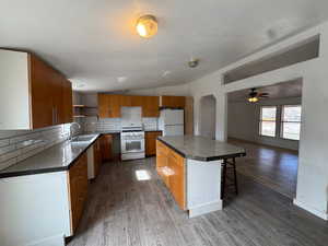 Kitchen with backsplash, tile counters, white appliances, a breakfast bar area, and vaulted ceiling
