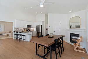 Dining space with light wood-style flooring, a fireplace with flush hearth, high vaulted ceiling, a ceiling fan, and recessed lighting