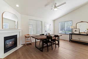 Dining area with vaulted ceiling, hardwood / wood-style flooring, a tile fireplace, and a ceiling fan