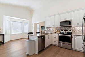 Kitchen featuring stainless steel appliances, white cabinetry, a peninsula, light stone countertops, and vaulted ceiling