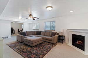 Living area with light colored carpet, a fireplace, a ceiling fan, a textured ceiling, and recessed lighting