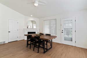 Dining area with light wood-style flooring, a fireplace, lofted ceiling, recessed lighting, and ceiling fan