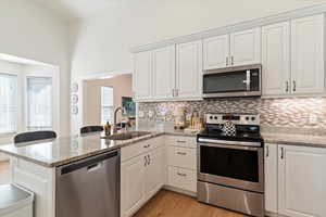Kitchen featuring appliances with stainless steel finishes, light stone counters, white cabinets, and a peninsula