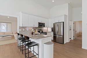 Kitchen with stainless steel appliances, light stone countertops, recessed lighting, white cabinetry, and a peninsula