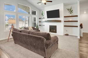 Living room with a large fireplace, a ceiling fan, high vaulted ceiling, light wood-type flooring, and recessed lighting