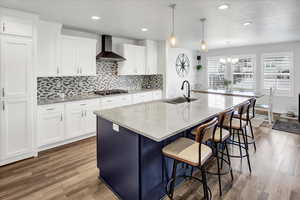 Kitchen with light stone counters, backsplash, white cabinetry, a breakfast bar area, and recessed lighting