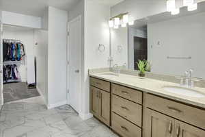 Bathroom featuring double vanity, light marble finish floors, and a spacious closet