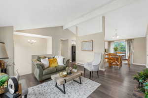 Living area with a chandelier, beamed ceiling, dark wood-style floors, and high vaulted ceiling