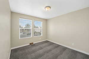 Spare room featuring dark colored carpet and baseboards