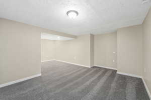 Spare room featuring dark carpet and a textured ceiling
